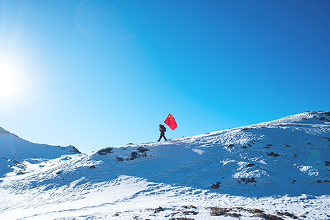 ◎ 在西藏山南市隆子縣玉麥鄉境內,護邊員普布羅布扛著國旗行走在雪坡上(二月六日攝)。